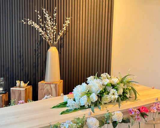 Wit rouwstuk op grafkist met bloemenband