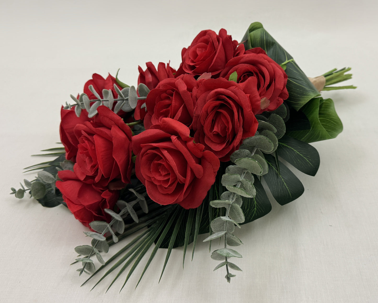 Liggend rouwboeket van rode rozen en eucalyptusbladeren