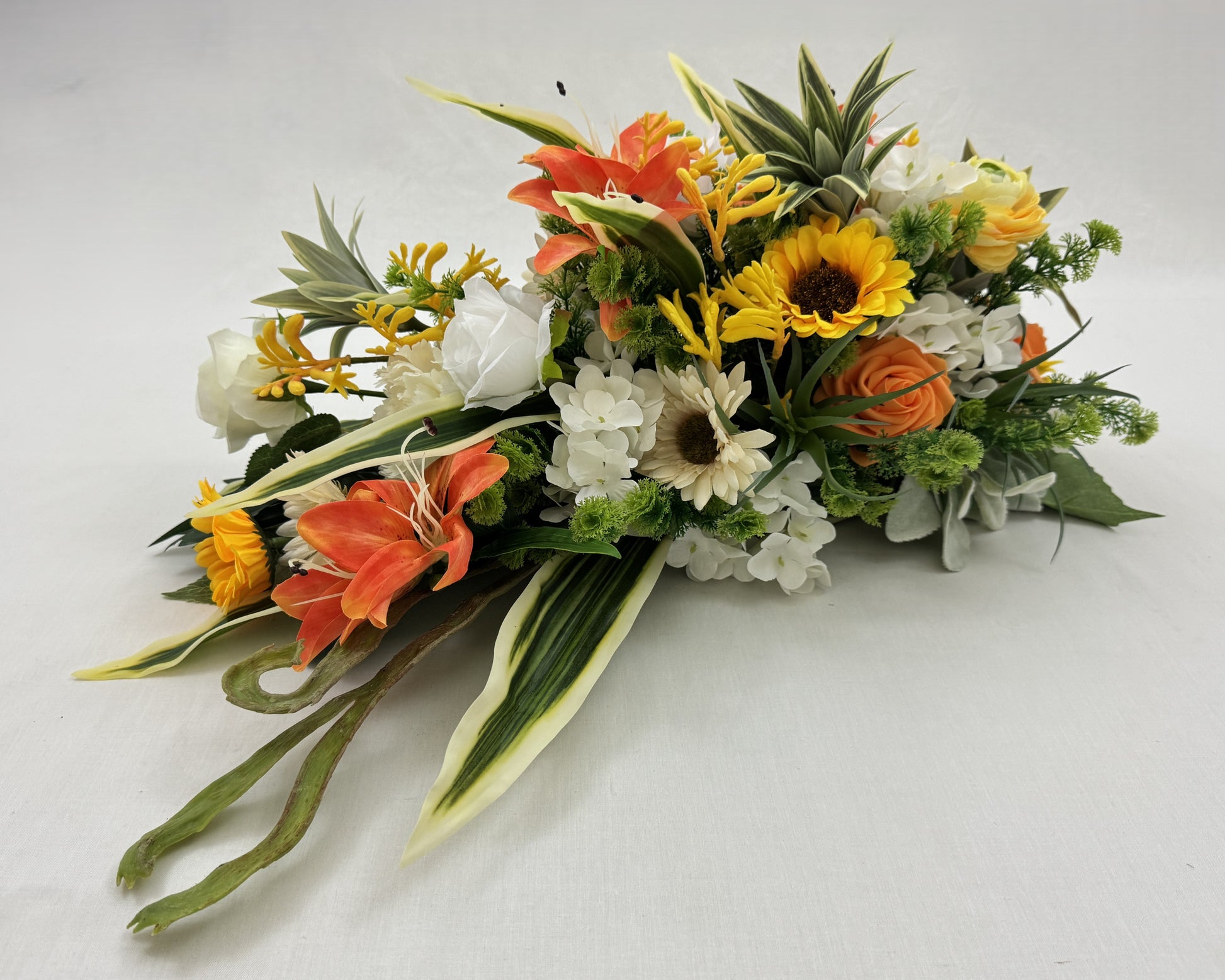 Druppelvormig rouwstuk met oranje en gele tinten. Zonnebloemen, lelies en rozen.