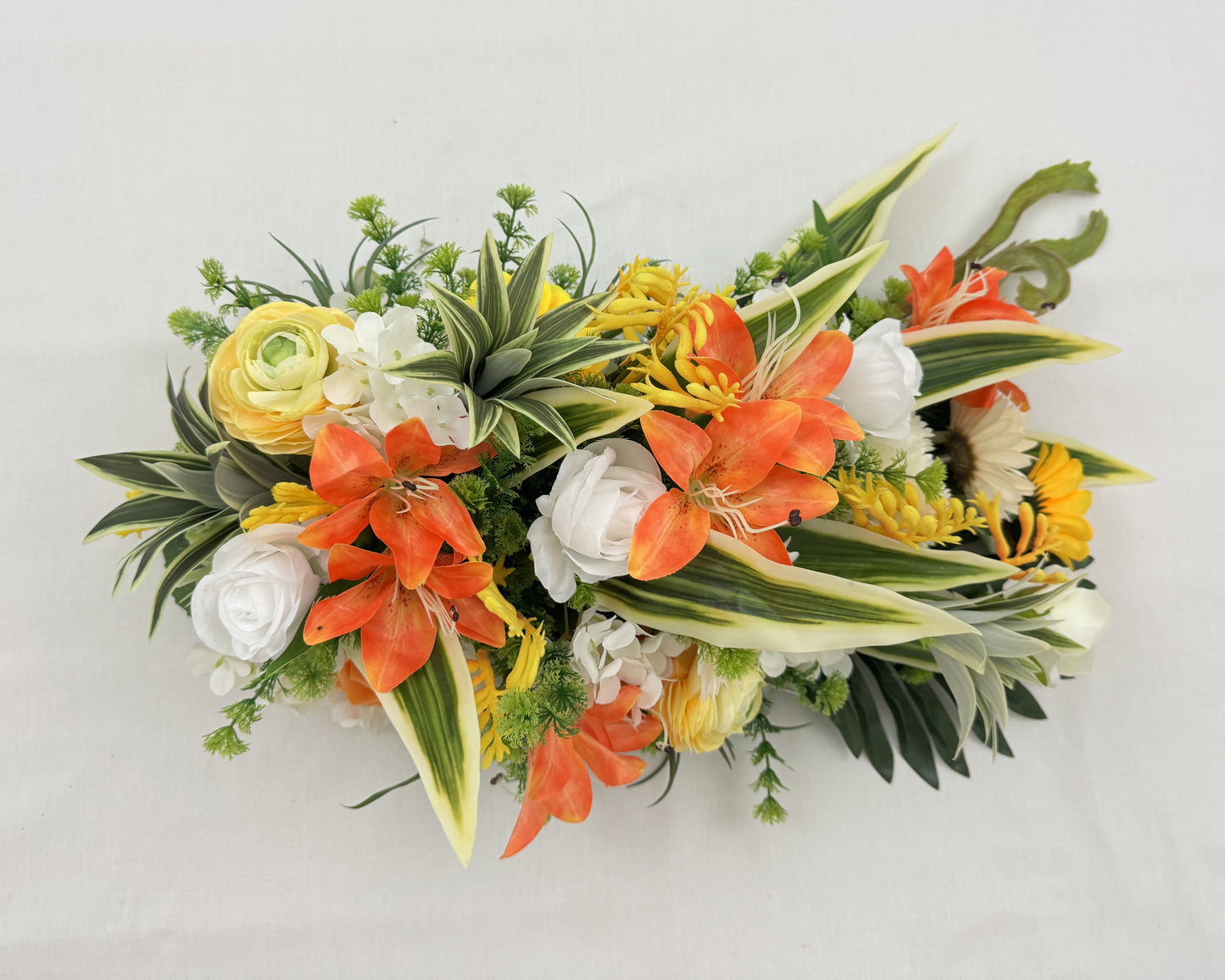 Druppelvormig rouwstuk met oranje en gele tinten. Zonnebloemen, lelies en rozen. Van boven getoond.