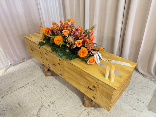 Rouwkist met oranje bloemstuk en kaarsjes erop