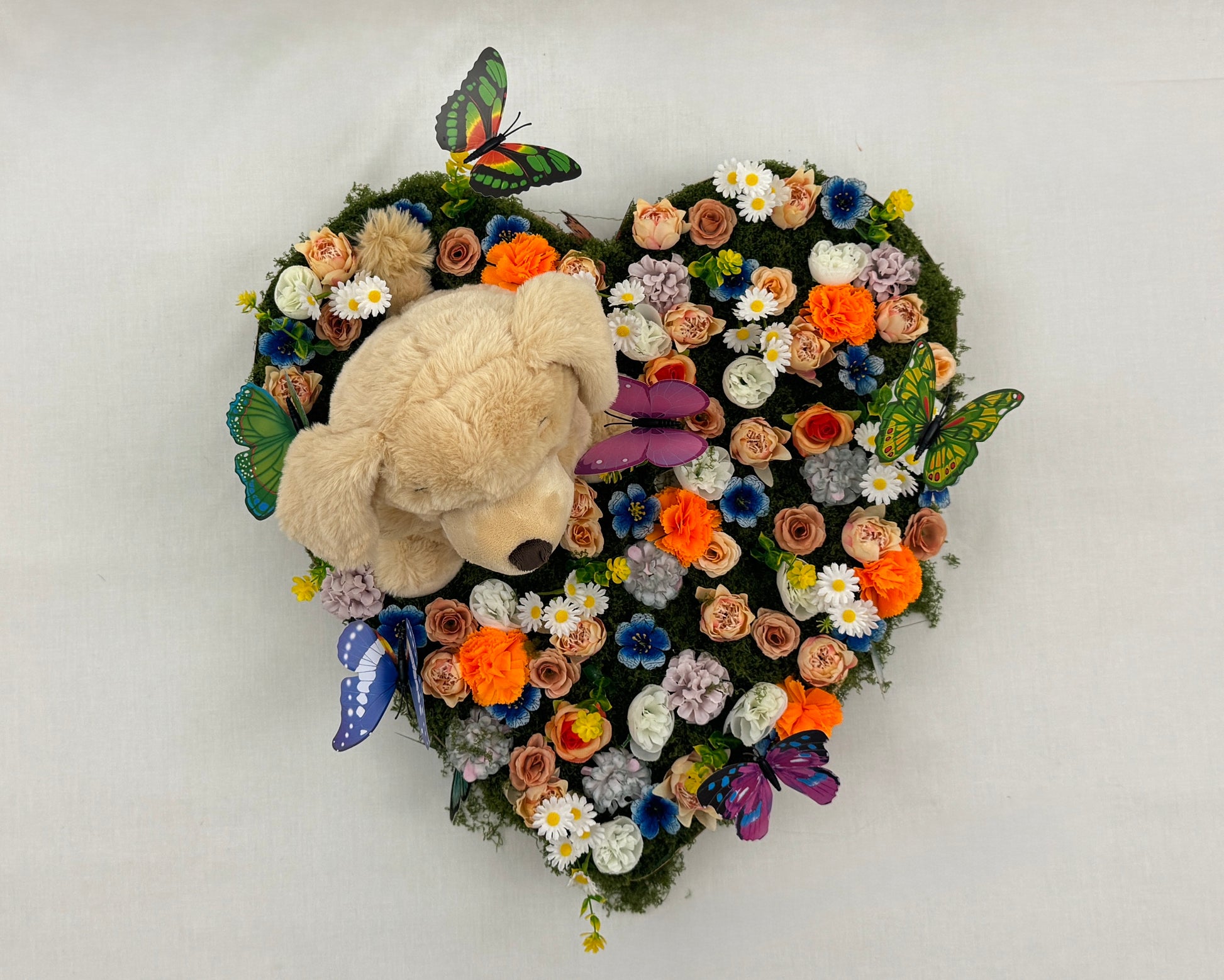 Rouwstuk voor kind met bloemen, vlinders en een teddybeer van boven gezien