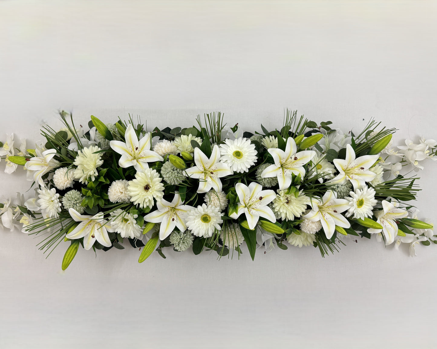 Langwerpig rouwstuk voor op de kist met witte lelies en gerbera's