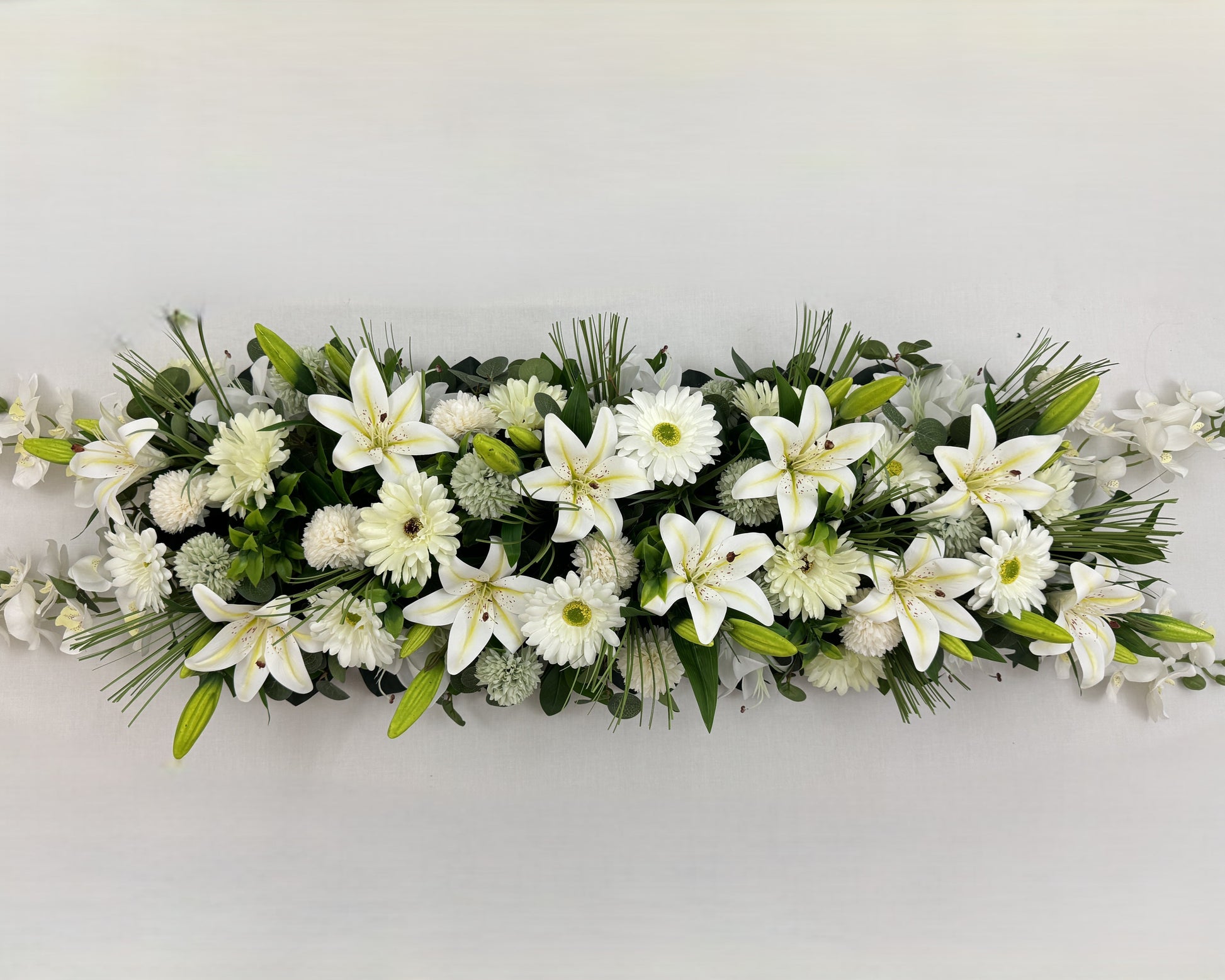 Langwerpig rouwstuk voor op de kist met witte lelies en gerbera's