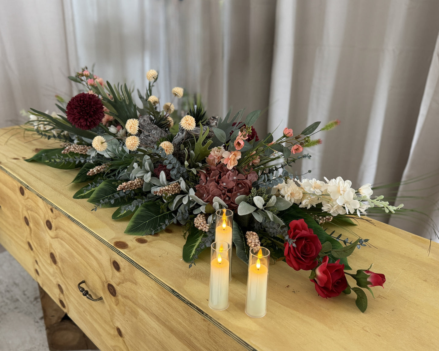 Kiststuk met hout en bordeauxrode bloemen met kaarsjes op de kist
