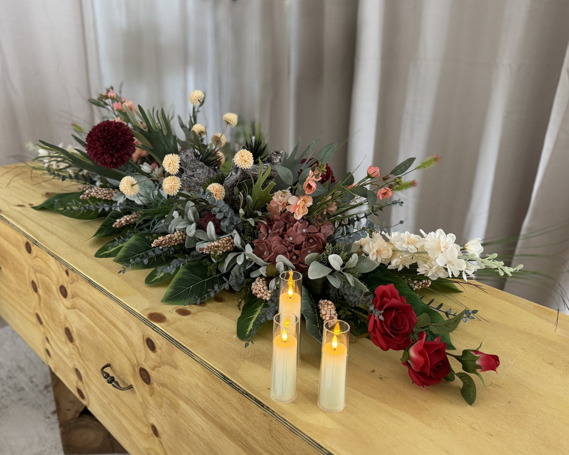 Kiststuk met hout en bordeauxrode bloemen met kaarsjes op de kist