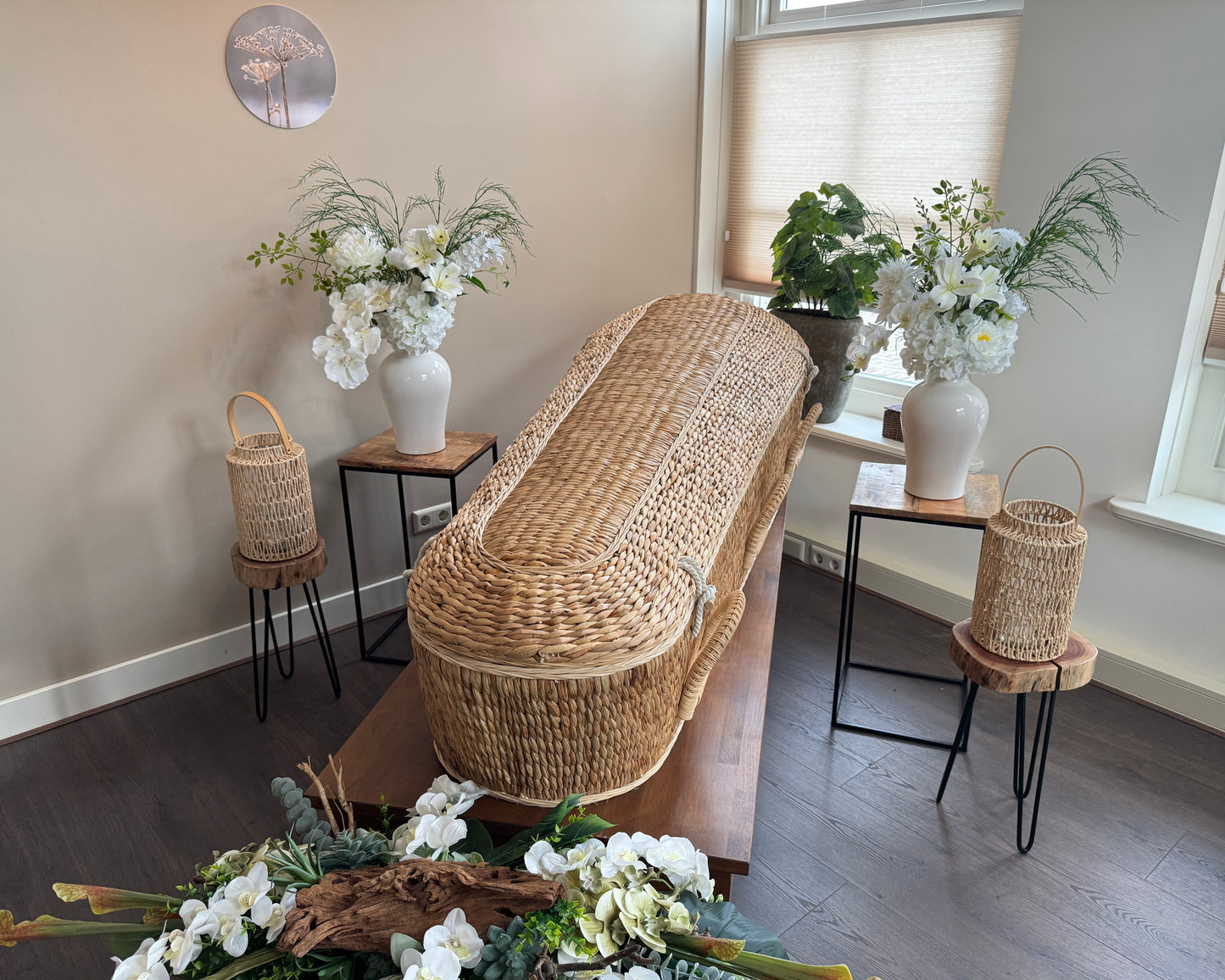 Rouwbloemen in vaas symmetrisch naast een grafkist van riet
