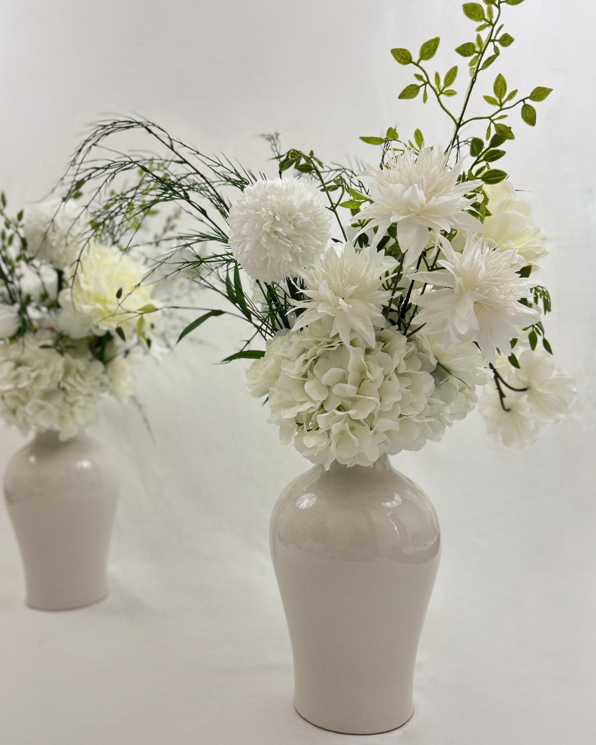 Twee identieke rouwboeketten voor naast de kist met witte bloemen in vaas