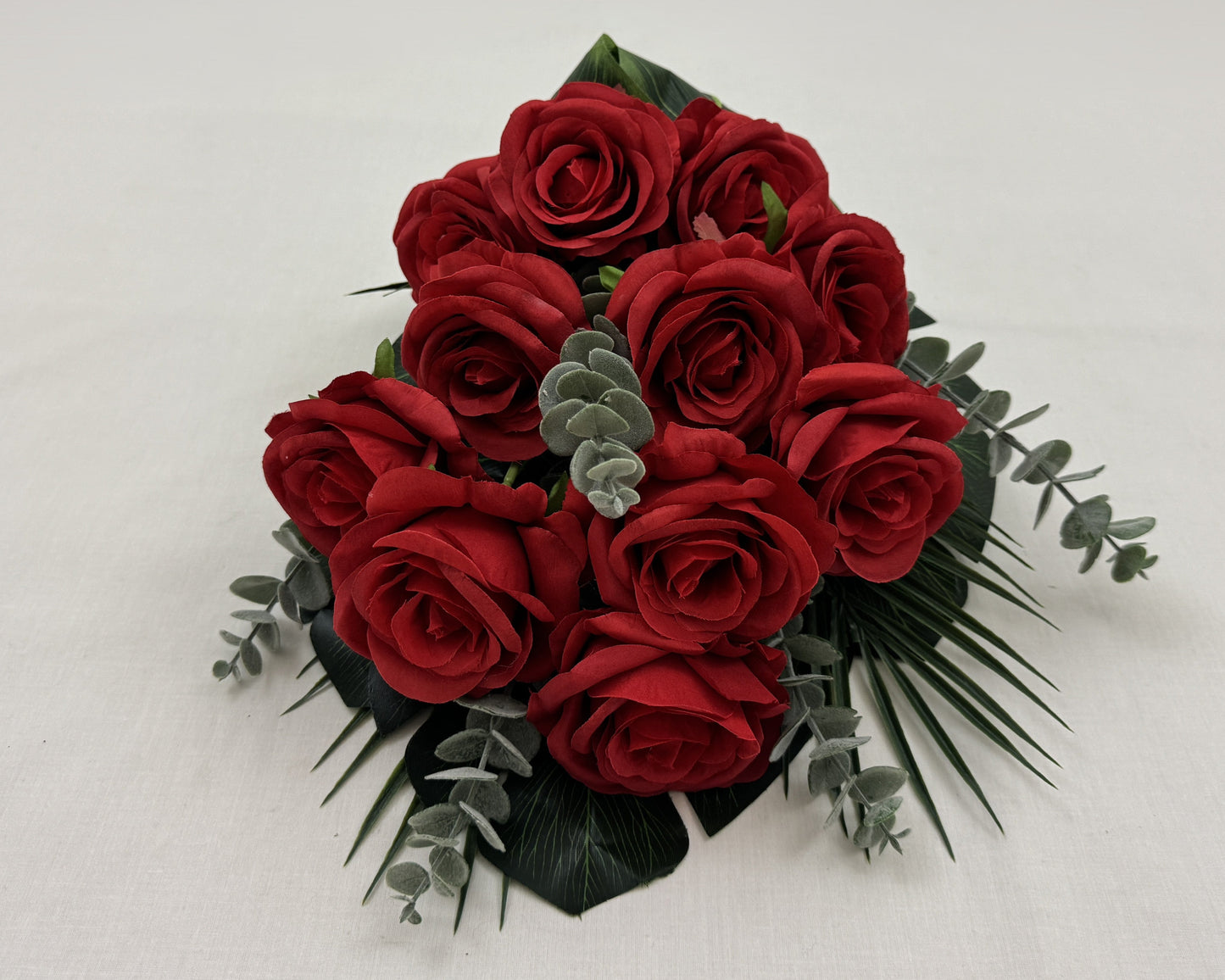 Liggend rouwboeket van rode rozen en eucalyptusbladeren getoond vanaf de voorkant