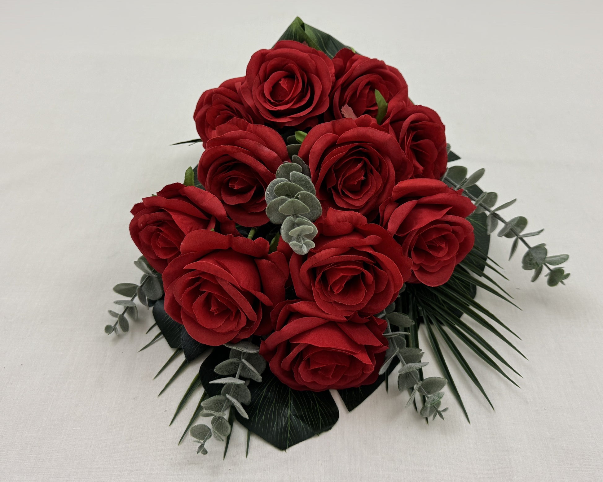 Liggend rouwboeket van rode rozen en eucalyptusbladeren getoond vanaf de voorkant